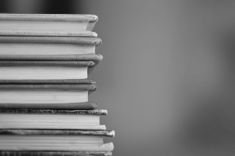 Une pile de livres aux bords usés, disposés verticalement sur un fond flou en noir et blanc.