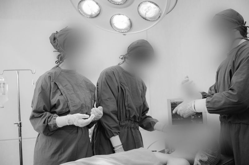 Surgical team in an operating room, wearing scrubs and masks, standing around a patient under bright overhead lights.