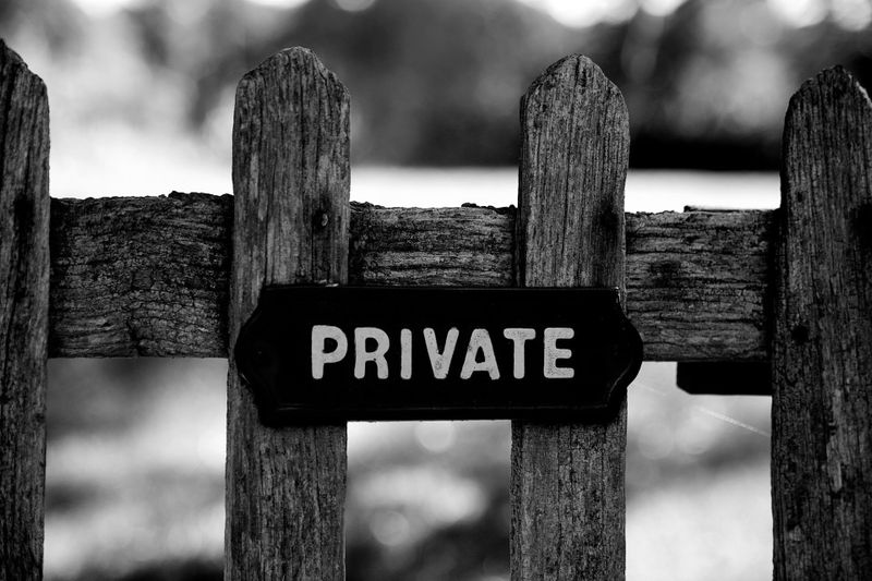 Clôture en bois patiné avec un panneau « PRIVÉ » en lettres blanches audacieuses, sur un fond naturel flou.