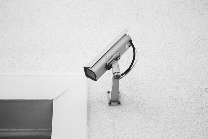 Une caméra de sécurité montée sur un mur blanc près du coin d'une fenêtre, capturant la zone en dessous.