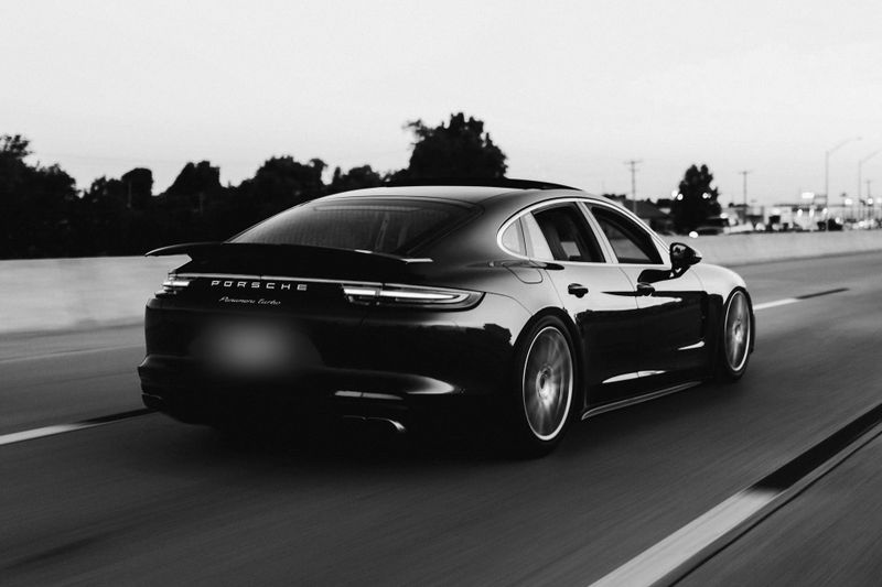 En la foto en blanco y negro se ve un coche de la marca Porsche, la matrícula ha sido anonimizada y está borrosa