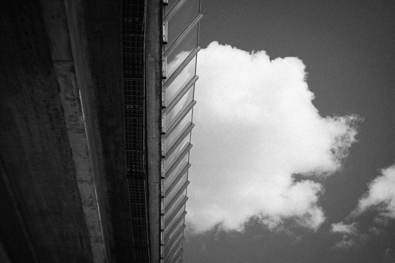 Image en noir et blanc d'une structure de pont à gauche, avec un gros nuage duveteux dans un ciel clair à droite.