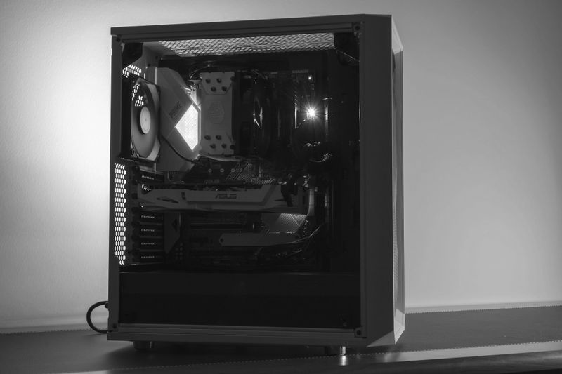 Una imagen en blanco y negro de una torre de computadora de escritorio con componentes interiores visibles, incluidos ventiladores y una tarjeta gráfica, iluminada desde un costado.