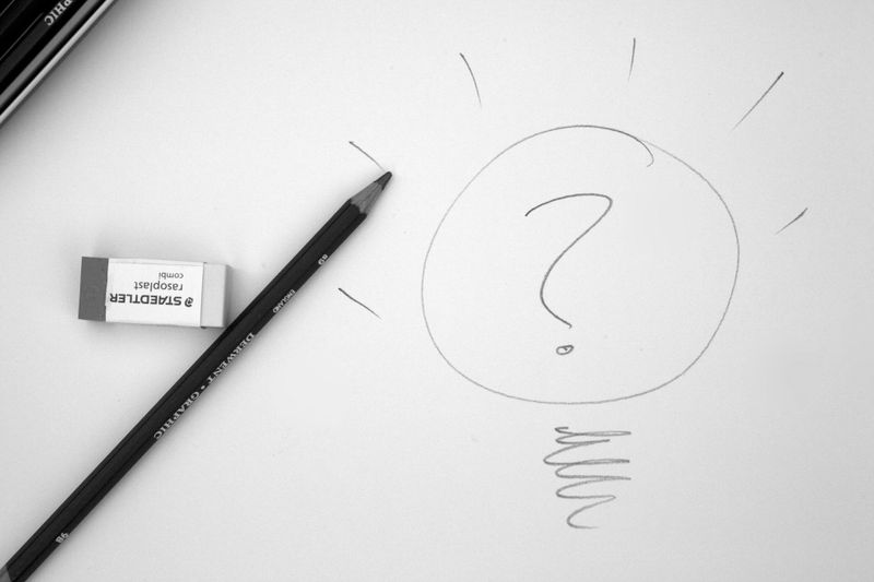 Crayon et gomme sur du papier avec un dessin d'ampoule contenant un point d'interrogation à l'intérieur, symbolisant un remue-méninges ou une idée.