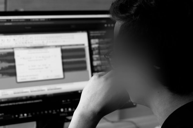 Personne devant un écran d'ordinateur affichant un logiciel de montage audio, vue de derrière en noir et blanc.