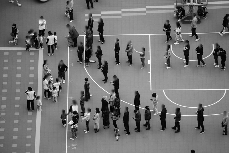 Aerial view of people standing in a long line on a basketball court, with others gathered nearby.