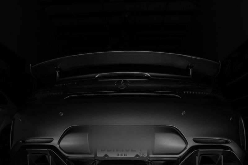 Close-up of a sleek, dark sports car rear with a prominent spoiler, photographed in low light, emphasizing its aerodynamic design.