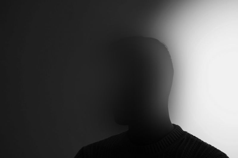 Silhouette of a person in a dimly lit setting, with light creating a gradient effect on the right side of the image.