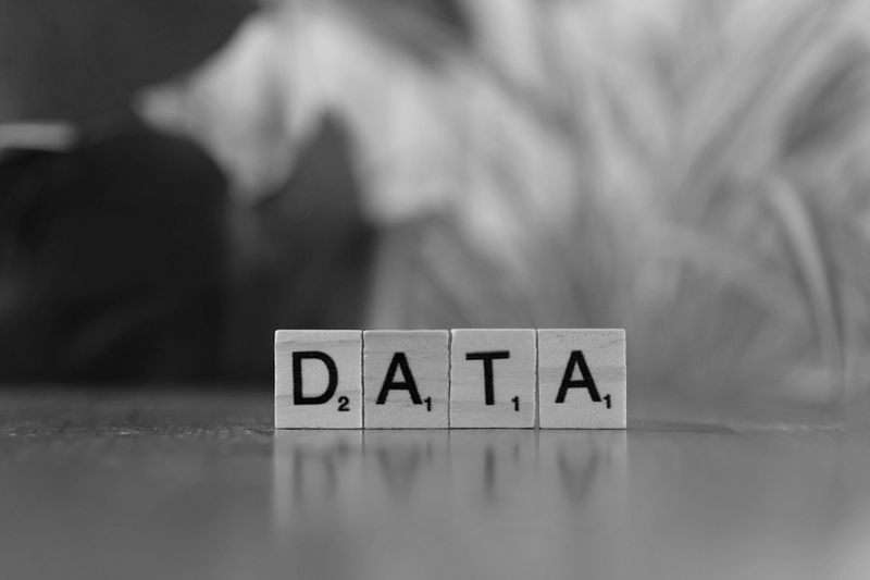 Tuiles de Scrabble avec le mot « DATA » sur une surface réfléchissante, avec un arrière-plan flou. Image en noir et blanc.