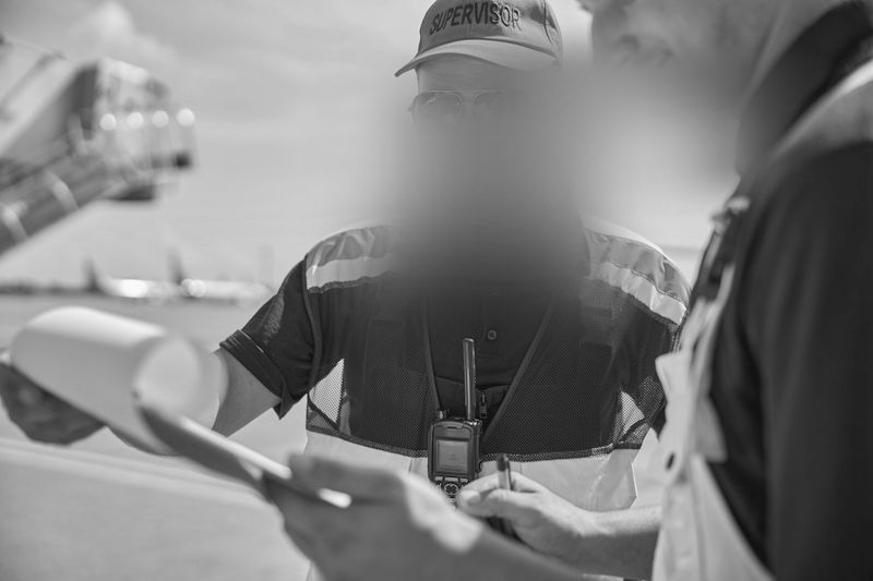 Fotografía en blanco y negro de dos trabajadores de la construcción en un proyecto con los rostros difuminados.