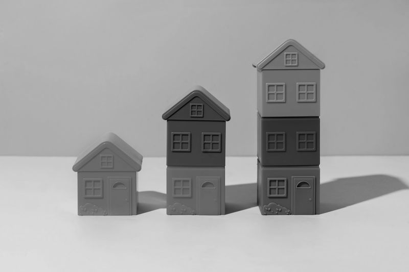 Image monochrome de trois piles de maisons miniatures, de taille croissante de gauche à droite, projetant des ombres sur une surface plane.