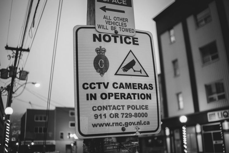 black-and-white photo of a 'CCTV cameras in operation' sign standing in the city