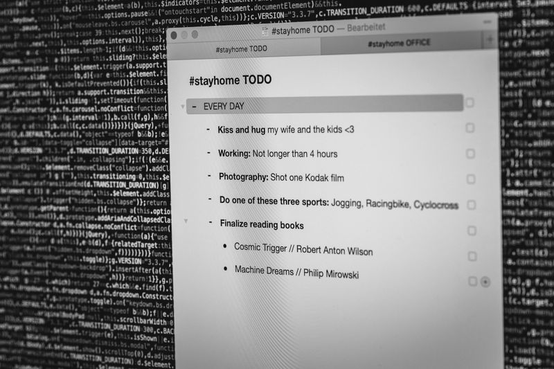 Sur l'écran de l'ordinateur, qui affiche un arrière-plan de code, une liste de tâches « stayhome » (rester à la maison) est visible, incluant des activités quotidiennes telles que les moments en famille, le travail, la photographie, le sport et la lecture.