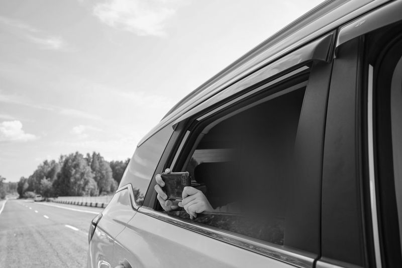 foto en blanco y negro de un coche desde un lateral a través de la ventana abierta, un pasajero con la cara anonimizada graba con el teléfono
