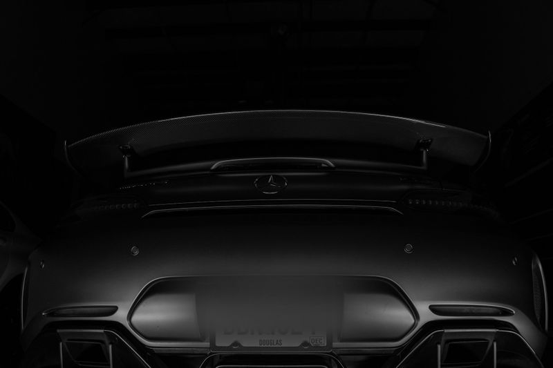 foto en blanco y negro de la parte trasera de un coche deportivo negro de la marca Mercedes con alerón, que tiene las matrículas difuminadas y borrosas