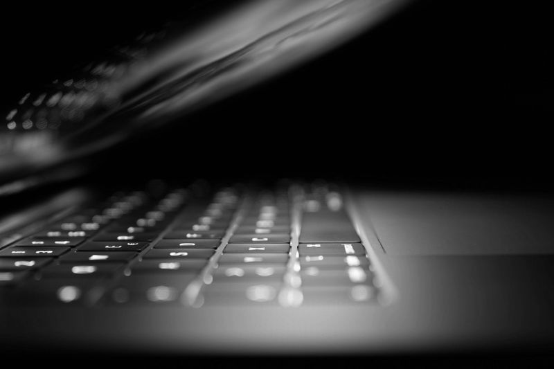 Gros plan d'un clavier d'ordinateur portable éclairé dans un environnement sombre, avec l'écran partiellement fermé, créant un effet d'éclairage spectaculaire.