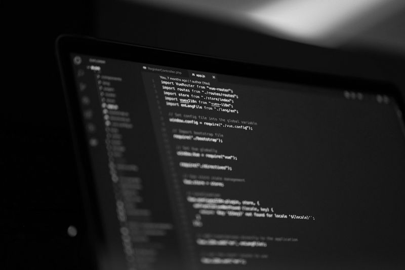 Primer plano en blanco y negro de la pantalla de un ordenador portátil que muestra líneas de código de programación en un editor de texto oscuro.