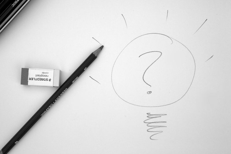 Ein Bleistift und ein Radiergummi neben einer Skizze einer Glühbirne mit einem Fragezeichen darin, was eine kreative oder innovative Frage symbolisiert.