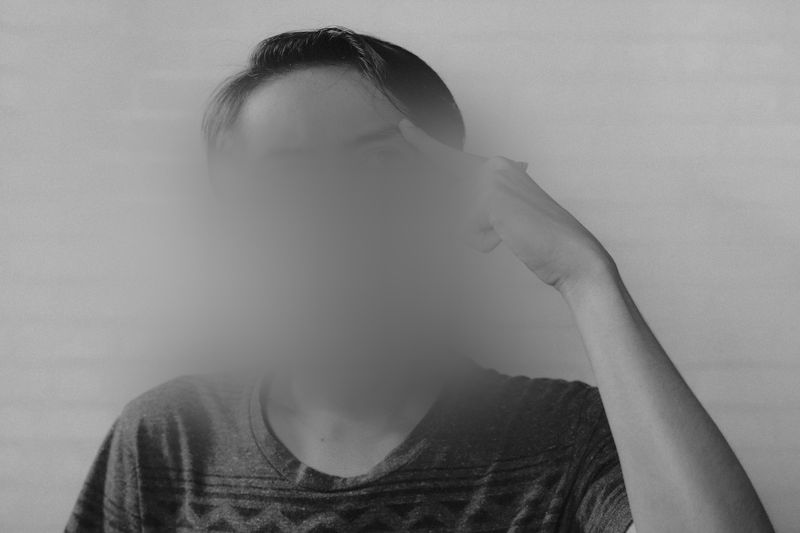 czarno-białe zdjęcie przedstawiające myślącego chłopaka, który opiera palec o skroń, ma zblurowaną twarz