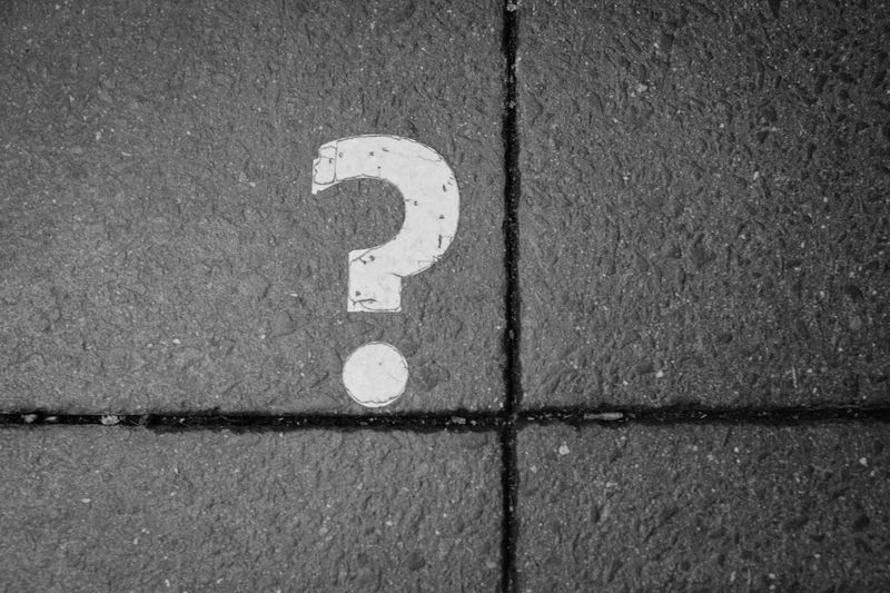 White question mark painted on dark tiled pavement.