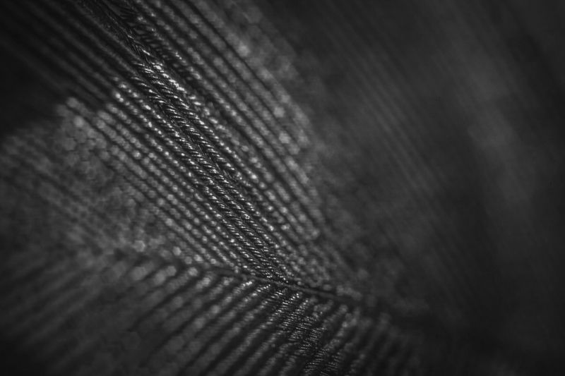 Close-up of a dark, textured fabric with diagonal lines and a sheen, creating a pattern of intersecting threads and subtle highlights.