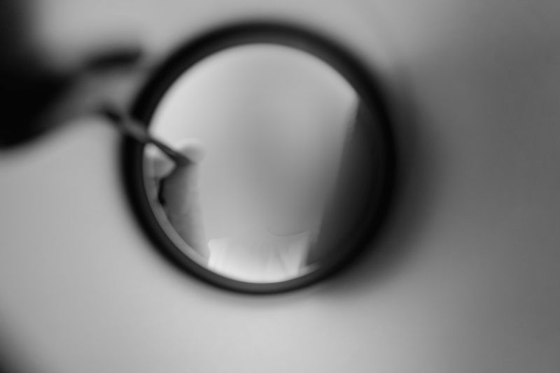 Blurred black-and-white image of a person applying makeup in a round mirror, creating an abstract and mysterious effect.
