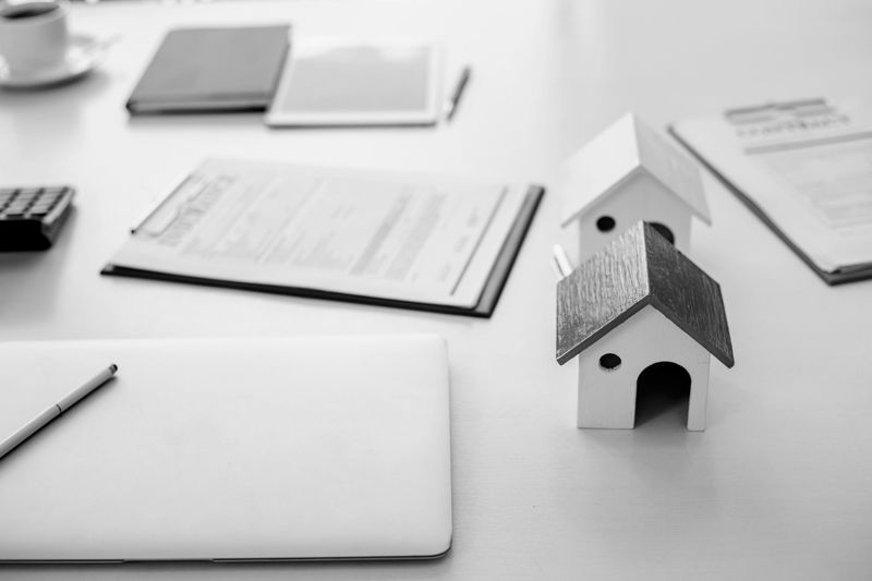 Petits modèles de maisons, documents, ordinateur portable et stylo sur un bureau, évoquant un espace de travail lié à l’immobilier ou à la planification financière.