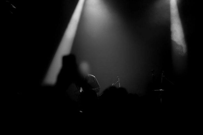 Silhouetted musician on stage under bright spotlights, with audience in the foreground.