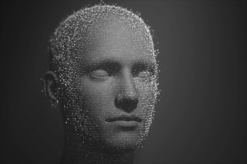 Un rendu 3D en niveaux de gris d'une tête humaine composée de nombreuses petites sphères, créant une apparence futuriste et numérique.