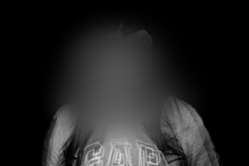 A person with a blurred face wearing a shirt with text, set against a dark background.