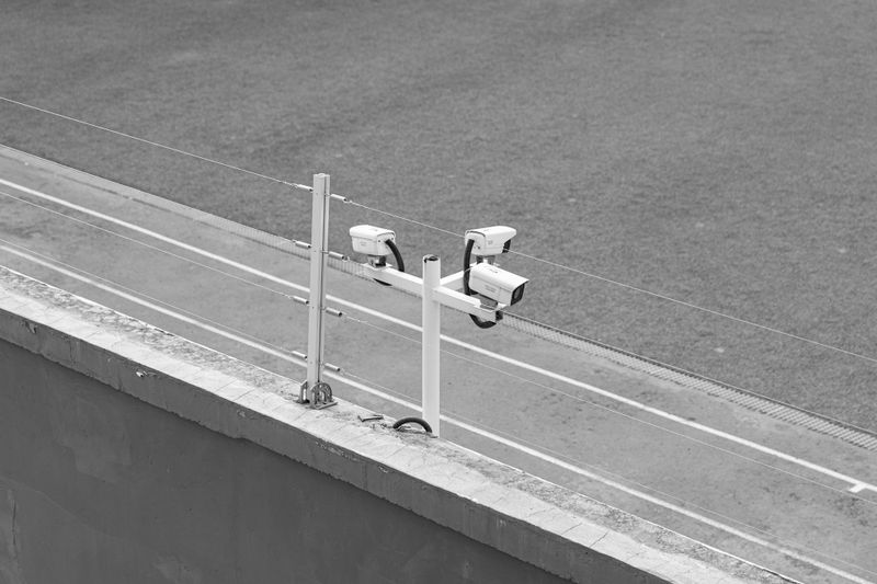 Dos cámaras de seguridad montadas en un poste con vista a un campo deportivo vacío, capturadas en blanco y negro.