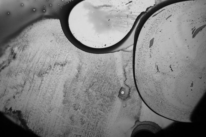 Close-up of abstract patterns with circular shapes and textured surfaces, resembling liquid or condensation on a window. Black and white.