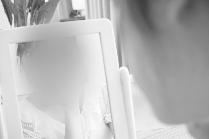 Black and white photo of a person looking into a mirror with their face blurred, surrounded by a softly lit interior.
