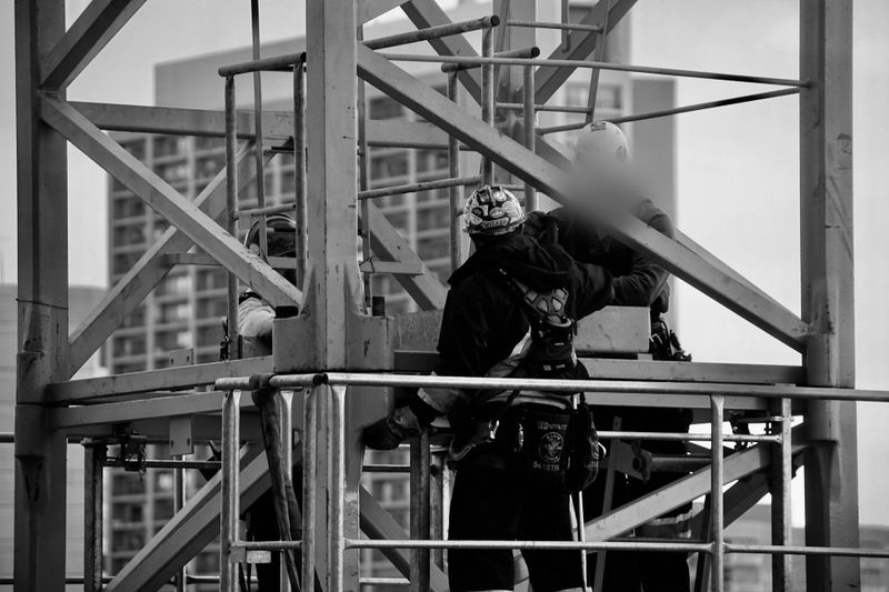 Trabajadores de la construcción con equipo de seguridad ensamblan una estructura de metal en un techo con edificios de la ciudad al fondo.