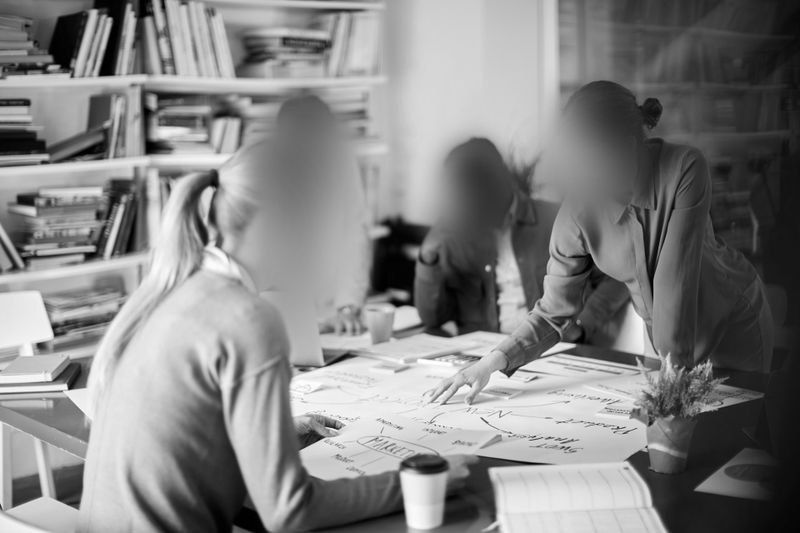 Groupe flou de personnes collaborant autour d'une table avec des papiers et des tasses à café, dans un cadre de bureau avec des étagères en arrière-plan.