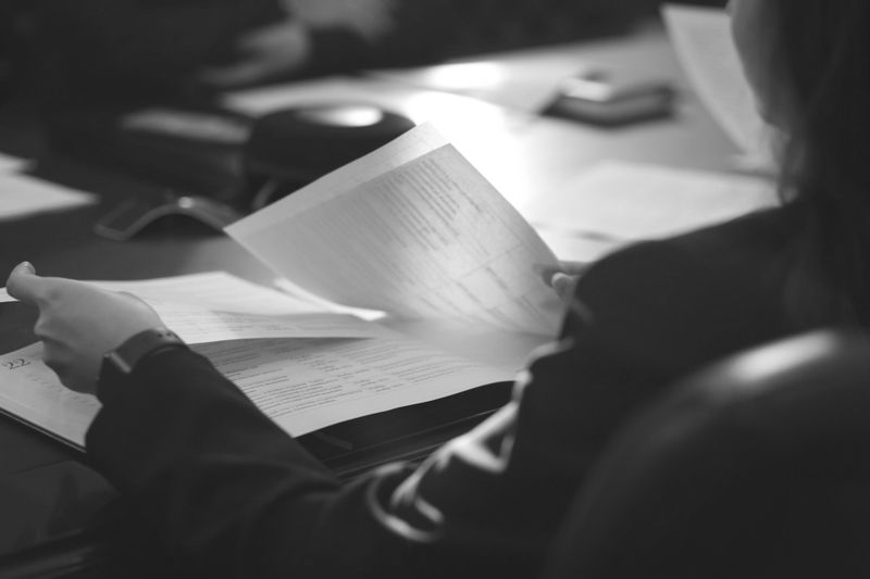 Personne tenant et examinant des documents à une table de réunion, avec un arrière-plan flou, suggérant un environnement professionnel.
