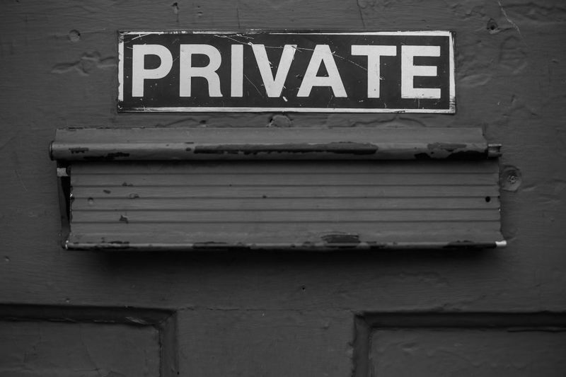 Image en noir et blanc d'une porte avec un panneau « PRIVÉ » au-dessus d'une fente à courrier fermée.