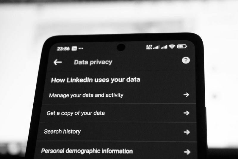 Primer plano en blanco y negro de un smartphone que muestra el menú «Privacidad de datos» de LinkedIn con opciones como «Gestionar tus datos» e «Historial de búsqueda».