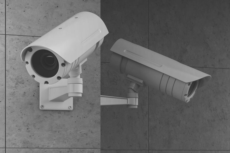 Image en noir et blanc d'une caméra de sécurité montée sur un mur carrelé, tournée vers la gauche.