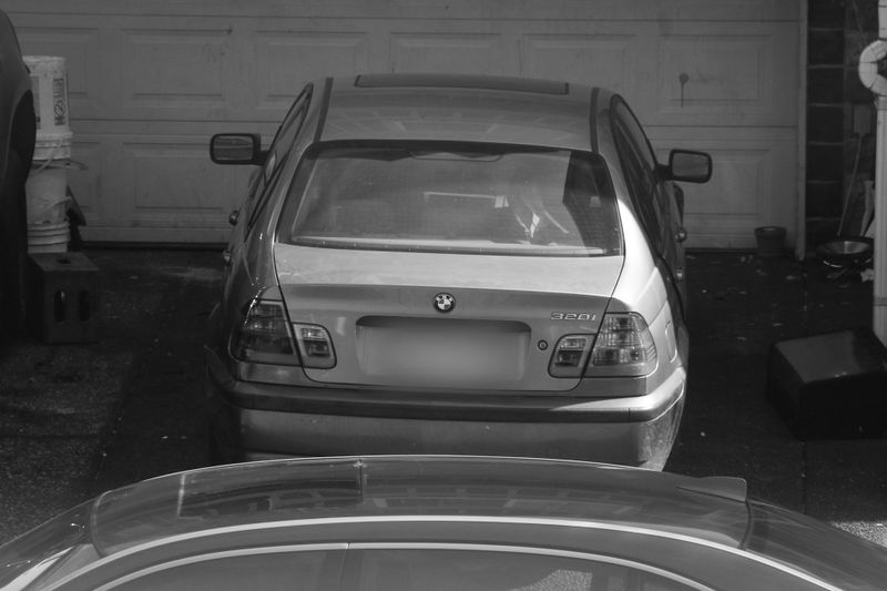 A black and white image of a parked BMW car viewed from the rear, with a garage door in the background.