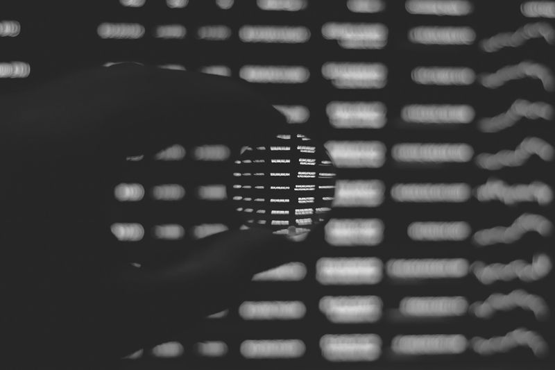 Silhouette einer Hand, die eine runde Linse hält, die einen Abschnitt verschwommenen Textes vor einem dunklen Hintergrund vergrößert.