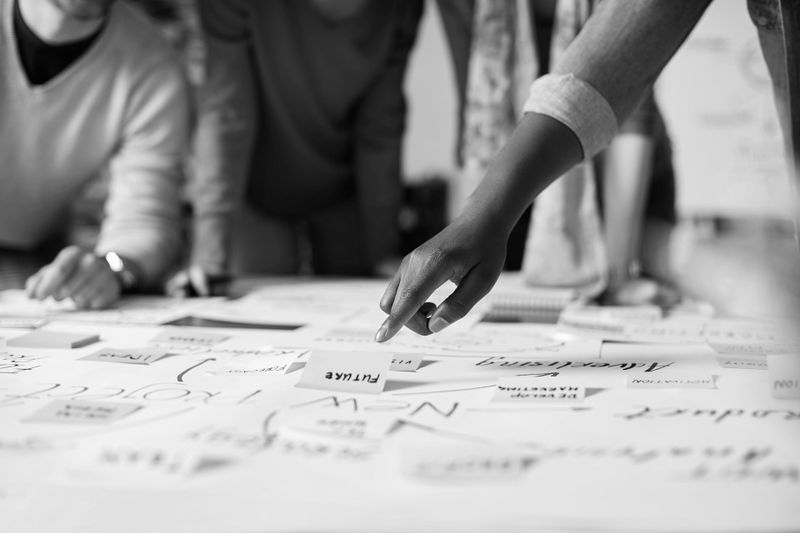 Des personnes collaborent autour d'une table, pointant du doigt des papiers contenant divers mots et diagrammes manuscrits, suggérant une séance de brainstorming.