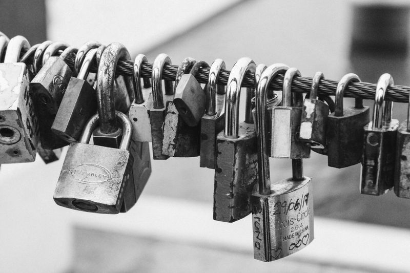 Photo en noir et blanc de nombreux cadenas attachés à un câble métallique, symbolisant la sécurité ou les cadenas d'amour sur un pont.