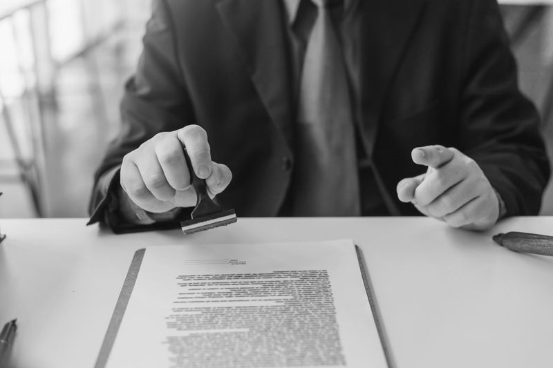 Person filling out a form with a pen, focusing on the signature section. The form is placed on a light-colored table.