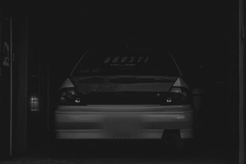 A car partially visible in a dimly lit garage, with "GHOST!" written on the rear window.
