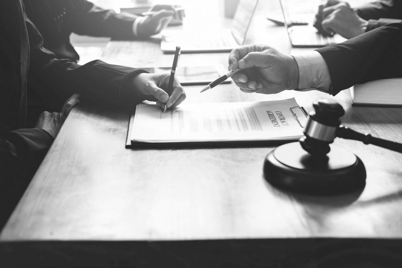 Personas en una reunión, discutiendo y señalando documentos sobre una mesa con un mazo cerca.