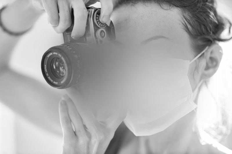 Une personne portant un masque facial et tenant un appareil photo devant son œil, semblant prendre une photo.
