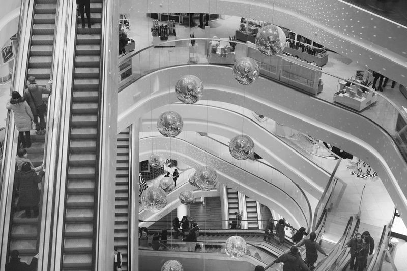 Bird's-eye view of a multi-level shopping mall with crisscrossing escalators, hanging mirrored spheres and shoppers on several floors.