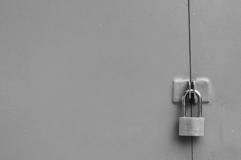 Porte en métal gris avec un cadenas pour la sécuriser, positionnée légèrement sur la droite. Apparence minimaliste et monochrome.