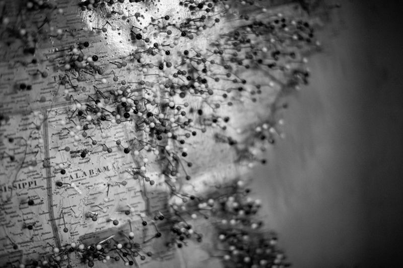 A black-and-white map of the southern US states, covered with numerous pushpins. Alabama is clearly visible, surrounded by a cluster of pushpins.